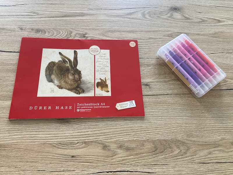 Ein Zeichenblock liegt auf einem Tisch, daneben einige Stifte